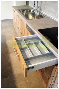 Η εικόνα απεικονίζει ένα τμήμα μιας σύγχρονης κουζίνας. Συγκεκριμένα, βλέπουμε ένα ανοιχτό συρτάρι ενός ξύλινου ντουλαπιού.